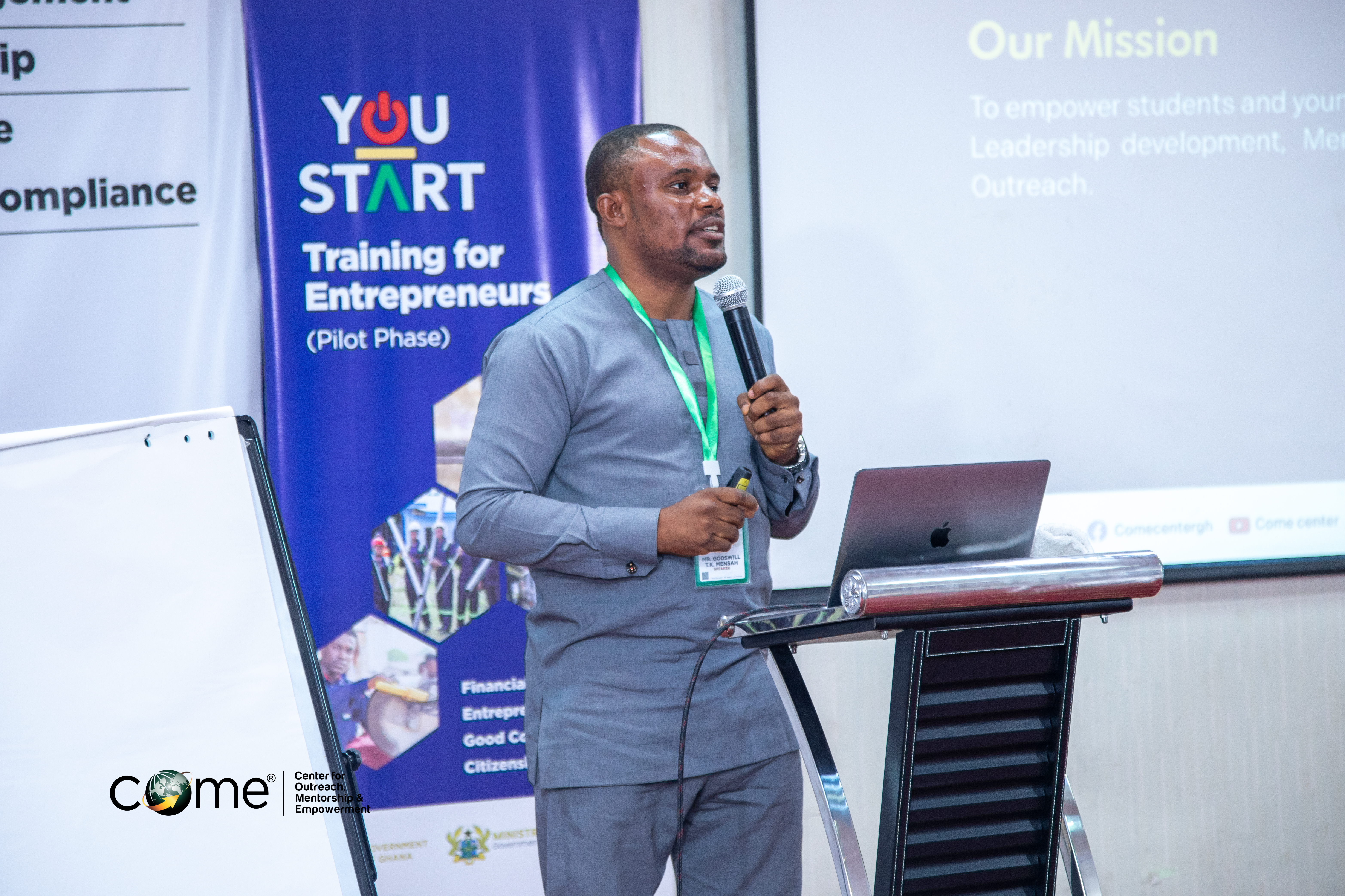 Bright campus-style building with reflective glass, trees, and red flowers in the foreground.